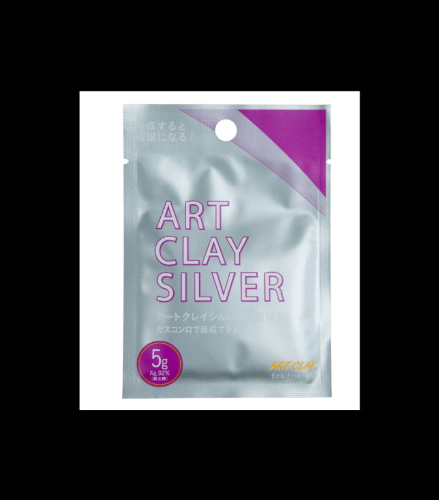 A 5g silver foil pouch of Art Clay Silver acrylic clay paste, featuring a metallic silver background with purple text and accents, and a purple circular badge indicating '5g'.